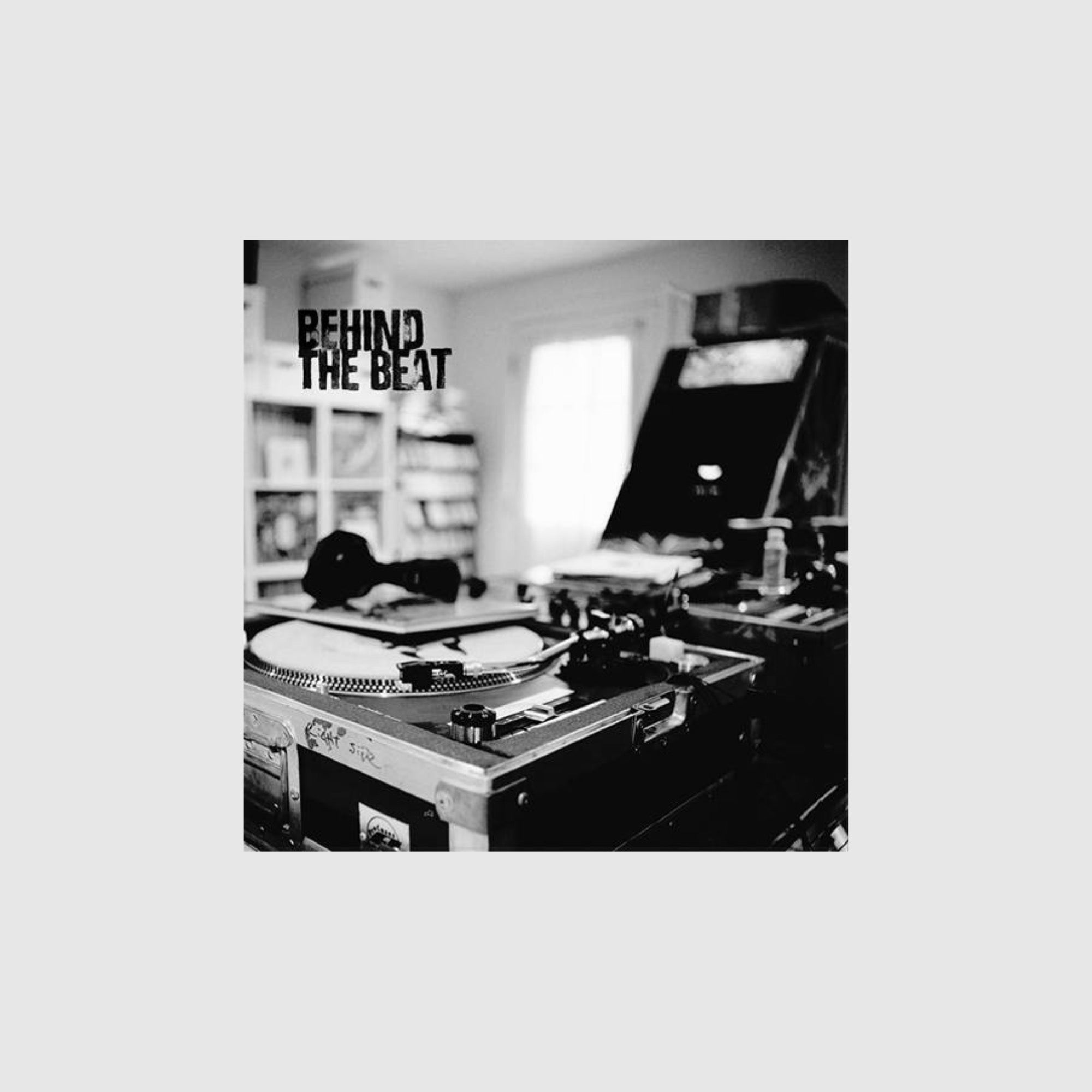 Gritty black and white photo of a turntable and vinyl collection, 'Behind The Beat' graffiti text.