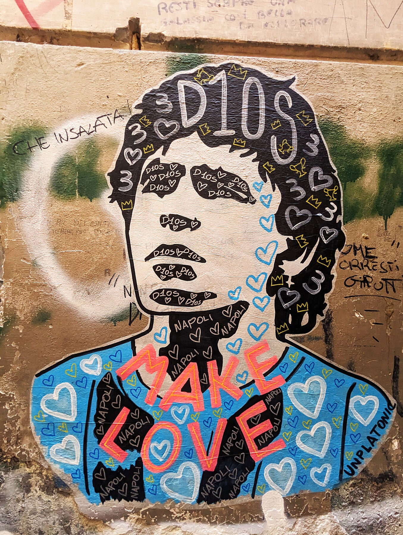 Street art of Diego Maradona in Naples featuring a stylized portrait with 'D10S' inscribed on his head, surrounded by hearts and the phrase 'MAKE LOVE' in bold red letters.
