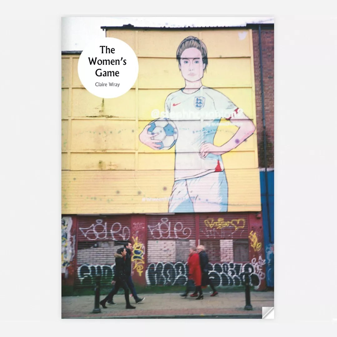 Cover of the zine "The Women's Game" by Claire Wray. The cover features a large mural of a female football player in an England football jersey holding a football, painted on a yellow wall. Below the mural, there is a row of shuttered storefronts with graffiti on the doors. Several people are walking along the sidewalk in front of the storefronts. The title "The Women's Game" and the author's name "Claire Wray" are displayed in a white circle in the upper left corner of the cover.